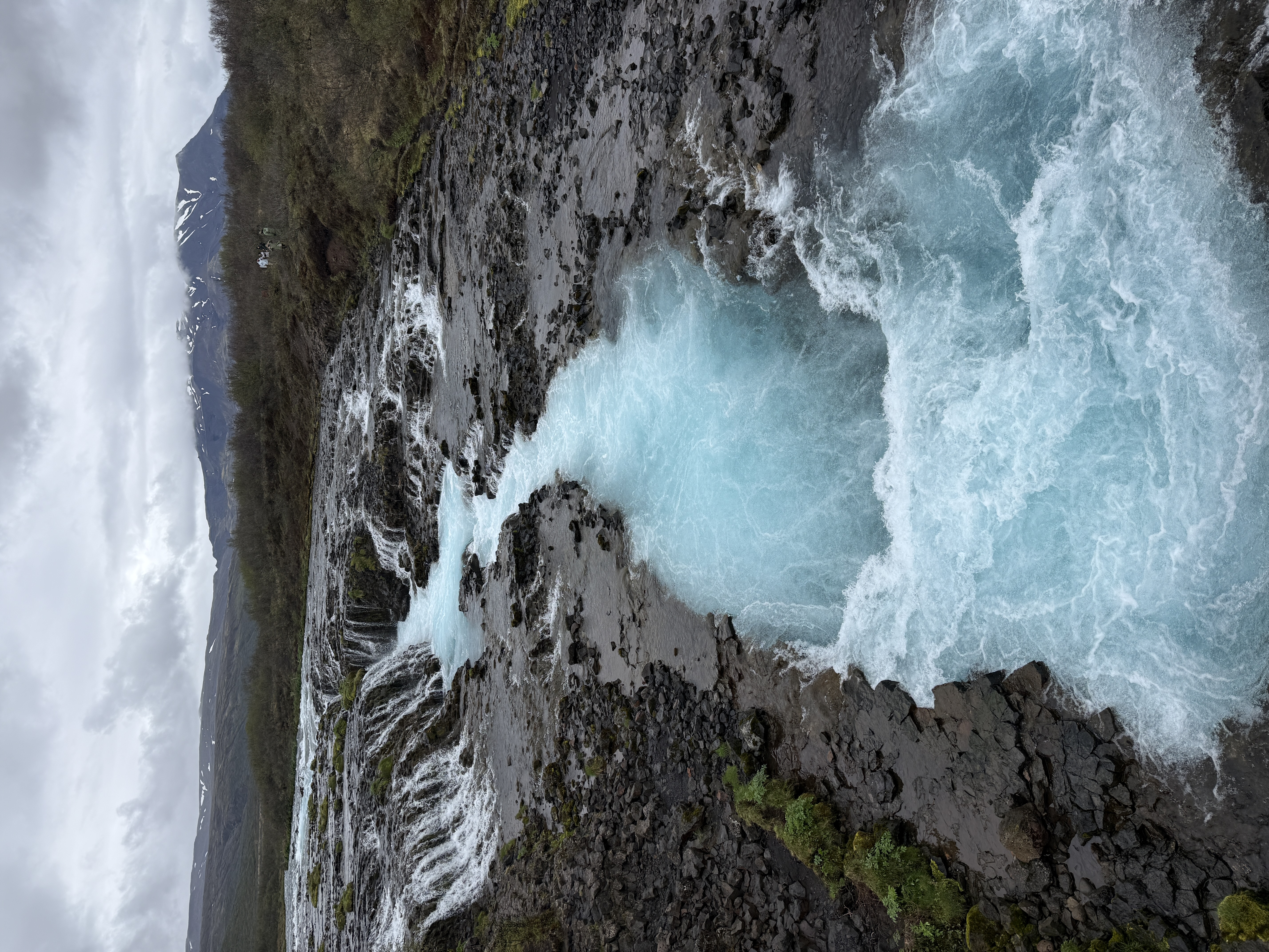 Glacier-blue water rushing through black volcanic rock in Iceland